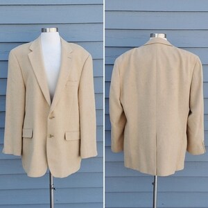 Peut inclure: Veste beige présentée sur un mannequin, avec vues avant et arrière. La veste a un revers cranté, deux boutons et deux poches avant. Le tissu semble doux et texturé.