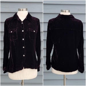 May include: A dark purple velvet button-down shirt with long sleeves and two chest pockets. The shirt is displayed on a mannequin, showcasing the front and back views. The fabric has a soft, textured appearance.
