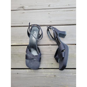 May include: A pair of black platform sandals with a square toe and ankle strap. The sandals have a block heel and the brand name "Mudd" is visible on the insole. The shoes are made of a satin-like material.