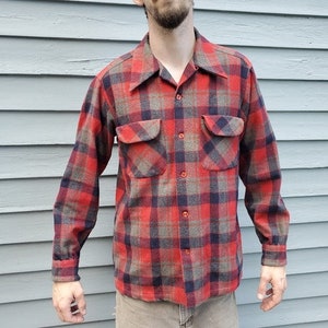 May include: A red, navy, and grey plaid flannel shirt with two chest pockets and a button-down front. The long-sleeved shirt has a classic collar and cuffs.