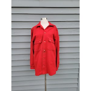 May include: A bright red long-sleeved shirt with a collared neckline and two chest pockets. The shirt has a button-down front and buttoned cuffs. The garment is displayed on a mannequin.