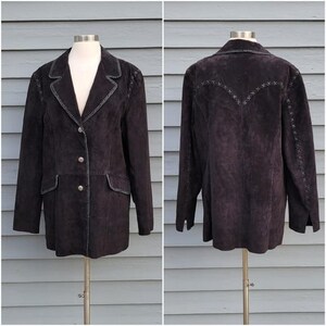 Puede incluir: Chaqueta de ante marrón oscuro con solapas, dos bolsillos delanteros y cierre de botones. La chaqueta presenta costuras decorativas a lo largo de las costuras y un diseño cosido en la espalda. La chaqueta se exhibe en un maniquí.