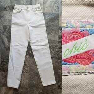 May include: Off-white denim jeans with a high waist and straight leg. The jeans have a classic five-pocket design and a button and zipper closure. A label with the word "chic" in green script is visible.