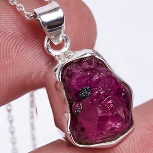 May include: A silver pendant necklace featuring a raw, pink ruby gemstone. The ruby is set in a silver bezel and has a rough, natural shape.