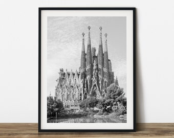 Peut inclure: Tirage encadré en noir et blanc de la Sagrada Família à Barcelone, Espagne. L'image met en valeur les détails architecturaux et les flèches de la basilique, avec un ciel nuageux en arrière-plan. L'impression est présentée sur une surface en bois.