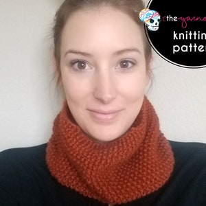 May include: A woman wearing a rust-coloured knitted cowl neck scarf. The scarf is made with a simple knit stitch and has a ribbed texture. The text "the yarnover knitting pattern" is visible in the background.