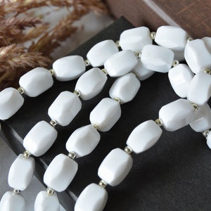 May include: A strand of white faceted beads with silver spacers. The beads are in a rectangular shape and are strung on a white cord.