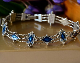 May include: A silver bracelet with a triple chain design and blue enamel diamond-shaped accents.