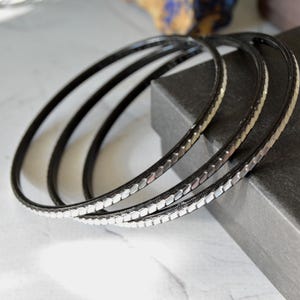 Peut inclure: Quatre bracelets argentés avec une finition émaillée noire. Les bracelets ont un motif décoratif de petits carrés argentés en relief.