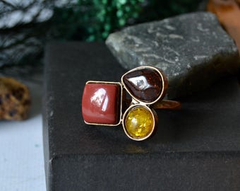 May include: A gold ring with three stones: a square red stone, a teardrop-shaped brown stone, and a round yellow stone.