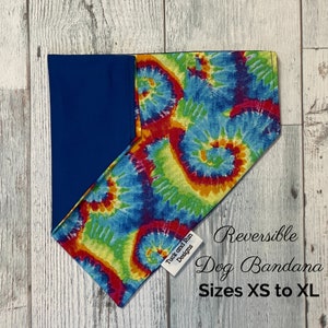 May include: Reversible dog bandana with a tie-dye pattern in shades of blue, green, yellow, orange, and red. One side is solid navy blue. The bandana is labelled "Tuck and Run Designs" and "Reversible Dog Bandana Sizes XS to XL".