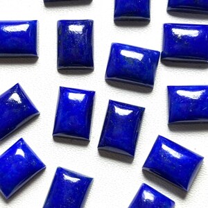 Può includere: Una collezione di pietre preziose rettangolari in lapislazzuli con una superficie lucida e liscia. Ogni pietra presenta un colore blu profondo e vibrante con sottili variazioni naturali e una finitura lucida, disposte in un motivo sparso.