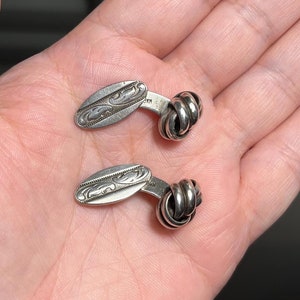 Puede incluir: Un par de gemelos de plata con un diseño de nudo y un patrón grabado.