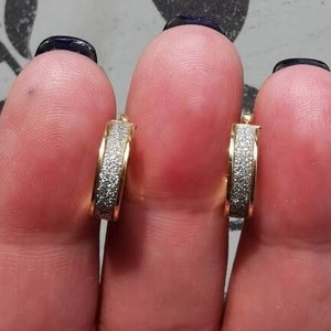 Puede incluir: Un par de pendientes de aro de oro con un acabado brillante. Los pendientes son pequeños y delicados.