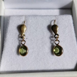 Puede incluir: Un par de pendientes de oro con gotas de piedras preciosas verdes en una caja blanca.