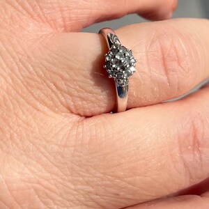 Puede incluir: Un anillo de plata con un grupo de peque&ntilde;as piedras preciosas redondas y transparentes. La banda del anillo es lisa y pulida, y las piedras est&aacute;n engastadas juntas, creando un efecto brillante. El anillo se muestra en un dedo.