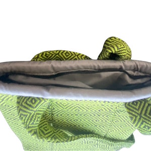 Puede incluir: Una bolsa de mano de color verde y negro con un forro gris. La bolsa est&aacute; abierta y el forro es visible.