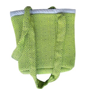 Puede incluir: Una bolsa de mano verde y negra con un patr&oacute;n de diamantes. La bolsa tiene dos asas largas y un forro blanco.