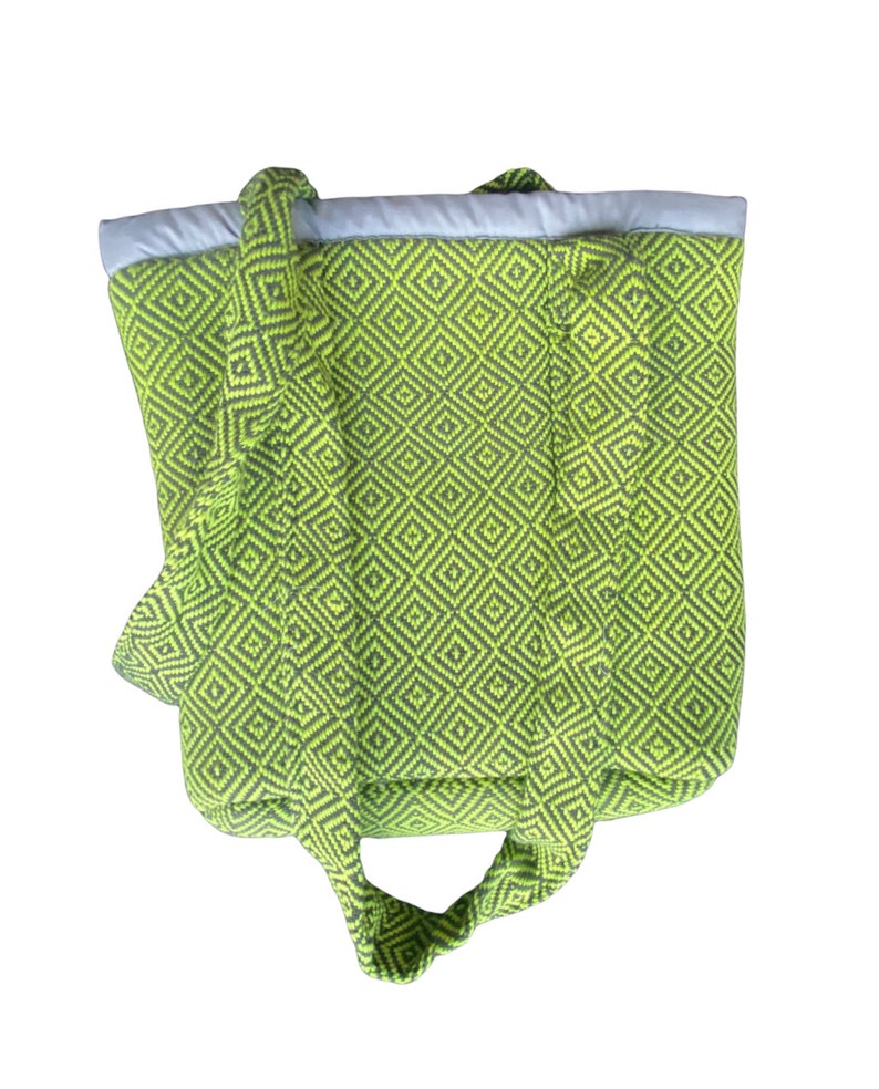 Puede incluir: Una bolsa de mano verde y negra con un patr&oacute;n de diamantes. La bolsa tiene dos asas largas y un forro blanco.