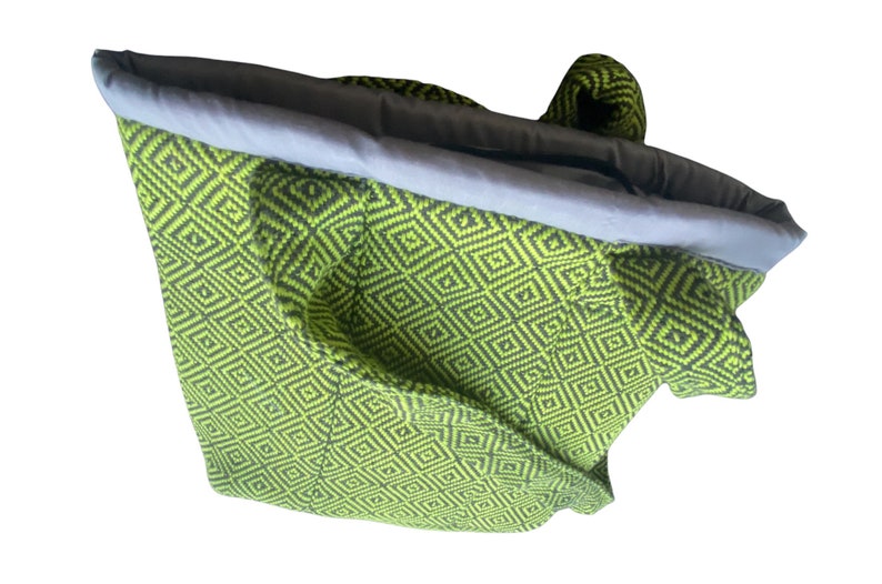 Puede incluir: Una bolsa de mano de color verde y negro con estampado geom&eacute;trico y forro de tela gris. La bolsa est&aacute; doblada y dada la vuelta.