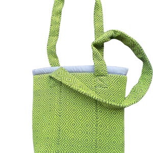 Puede incluir: Una bolsa de mano verde con un patr&oacute;n geom&eacute;trico. La bolsa tiene una sola correa que se puede llevar sobre el hombro.