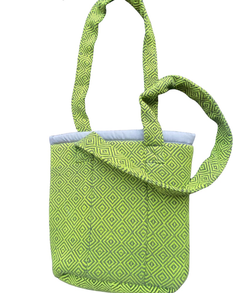 Puede incluir: Una bolsa de mano verde con un patr&oacute;n geom&eacute;trico. La bolsa tiene una sola correa que se puede llevar sobre el hombro.