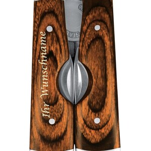 Könnte beinhalten: Ein Multitool mit Holzmaserung und dem eingravierten Text "Ihr Wunschname" auf dem Griff. Das Werkzeug ist geschlossen und hat eine silberne Oberfläche.