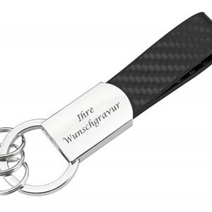 Könnte beinhalten: Ein schwarzer Leder-Schlüsselanhänger mit einem silbernen Schlüsselring und einer silbernen Plakette mit der Aufschrift "Ihre Wunschgravur".