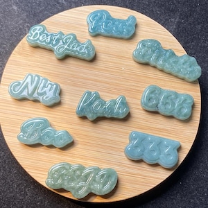 May include: A collection of ten jade pendants with various words and numbers carved into them. The pendants are displayed on a wooden surface.