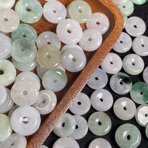 Puede incluir: Una colección de cuentas de jade verde y blanco en forma de rosquilla con un agujero en el centro. Las cuentas están dispuestas sobre una superficie de madera y un fondo negro.