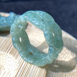 May include: A green jade ring with a braided design. The ring is made of a smooth, polished jade and has a light green color.