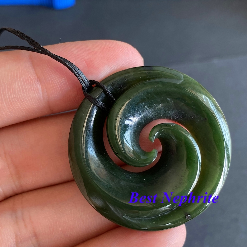 May include: A green jade pendant with a spiral design, known as a Maori Hei Tiki, on a black cord.
