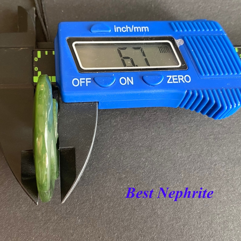 May include: A close-up of a green jade pendant being measured with a digital caliper. The caliper reads 6.7 mm. The text "Best Nephrite" is visible below the pendant.