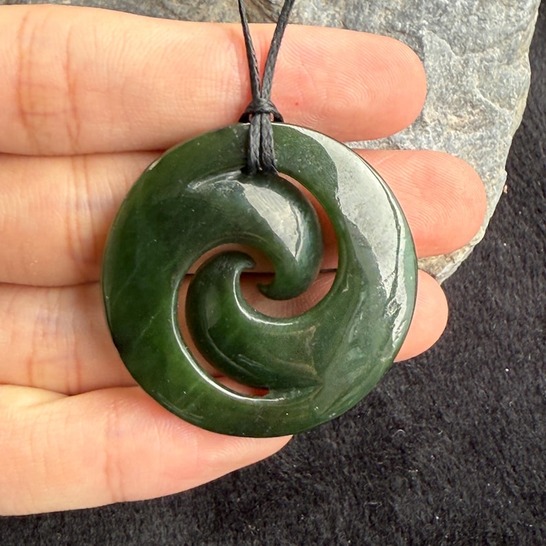 May include: A green jade pendant with a spiral design, hanging from a black cord.