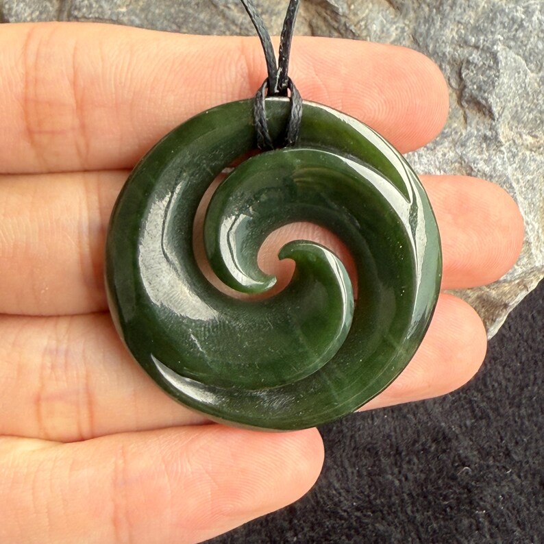 May include: A green jade pendant with a spiral design, hanging from a black cord.