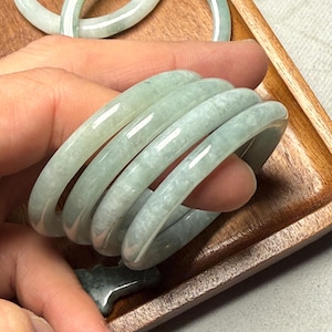 Pode incluir: Quatro pulseiras de jade verde empilhadas umas sobre as outras. As pulseiras são lisas e polidas.