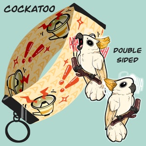May include: Double-sided Cockatoo design on a yellow and white lanyard with a red exclamation point pattern. The lanyard has a black metal clip and a silver key ring. The Cockatoo is white with a yellow crest and is shown with its mouth open as if it is screaming.