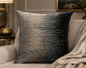 May include: A square throw pillow featuring a dense, textured surface of small beads. The design displays a gradient color transition, shifting from a metallic gold tone on the left side to a solid, deep black on the right side of the pillow.