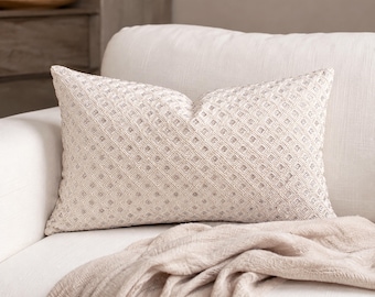 May include: A rectangular throw pillow featuring a cream-colored fabric base with a repeating diamond pattern. The design is composed of small, metallic silver beads stitched into the fabric, creating a textured, grid-like appearance across the surface.