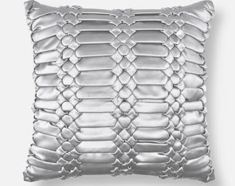 May include: A square throw pillow in a metallic silver color featuring a complex woven ribbon pattern across the entire front surface. The design consists of horizontal satin-like strips interlaced with vertical segments, creating a textured grid.