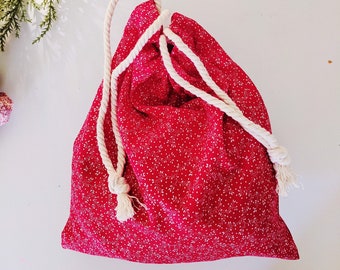 May include: A red drawstring bag with a white floral pattern. The bag is made of fabric and has a white cotton rope drawstring.