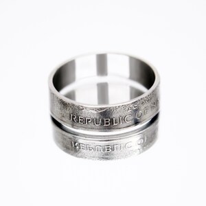 May include: Silver ring made from a US quarter coin. The ring is engraved with the words "Republic of N" on the outside of the band.