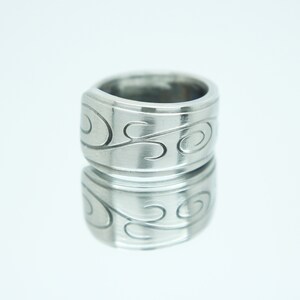 May include: A silver ring with a swirling design. The ring is wide and has a smooth, polished finish.