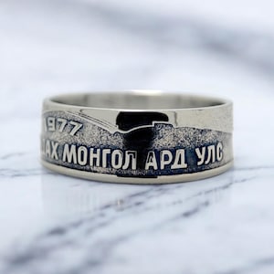 Può includere: Un anello d'argento con l'iscrizione "1977 АХ МОНГОЛ АРД УЛС" sulla fascia.