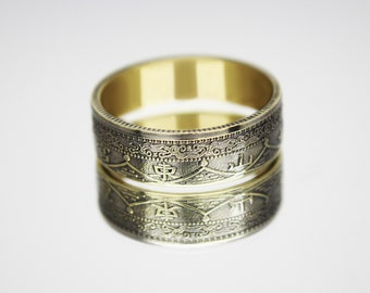 Könnte beinhalten: Ein goldener Ring aus zwei übereinander gestapelten japanischen Münzen. Die Münzen zeigen komplizierte Designs und japanische Schriftzeichen.