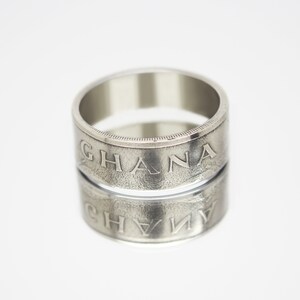 May include: A silver ring made from a Ghanaian coin. The ring is engraved with the word "GHANA" on both sides.