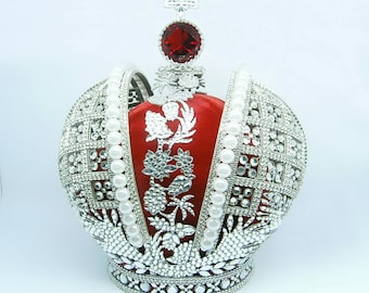 May include: A silver crown with a red jewel on top and a red velvet lining. The crown is decorated with white pearls and rhinestones.