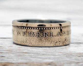 May include: A gold-toned ring made from a Dutch coin. The ring features the inscription "DE NEDERLAND" around the band.