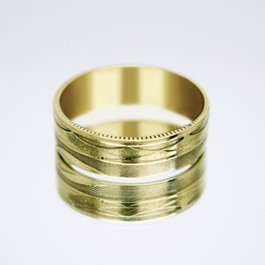 May include: A gold band ring with a textured design. The ring is made of a shiny metal and has a simple, classic style.