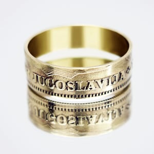 May include: A gold-coloured ring with the inscription "JUGOSLAVIJA" engraved around the band.
